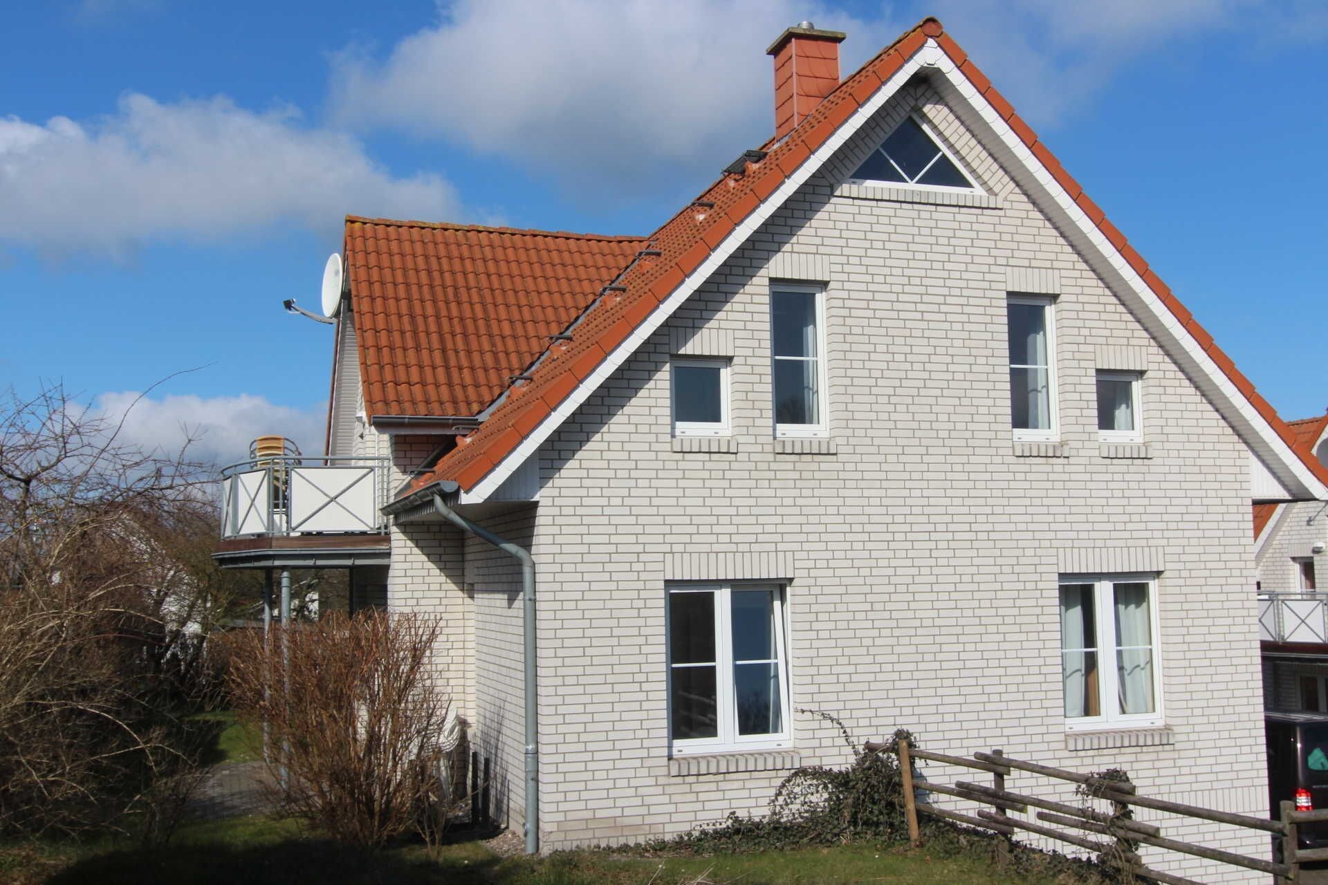 Een herenhuis met een rode dakbedekking, witte bakstenen muren en meerdere ramen.