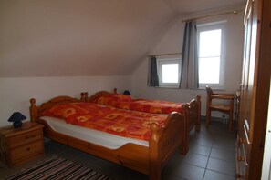A bedroom with two wooden beds, a nightstand, a chair, a window with curtains, and a radiator.