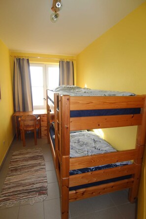 Una habitación con literas, un escritorio, una silla y un ventanal con cortinas.