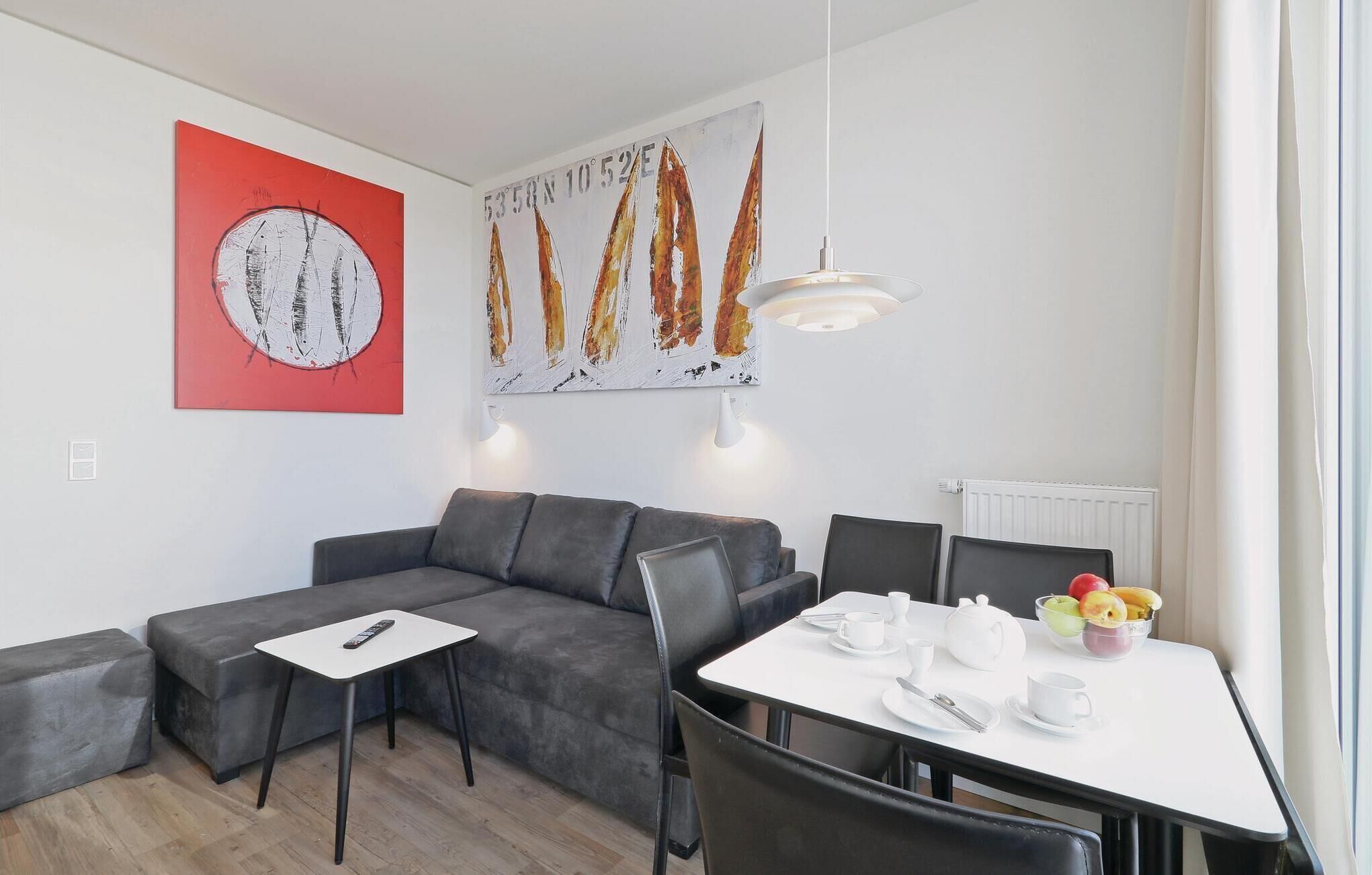 Una sala de estar moderna con un sofá seccional gris, una mesa de comedor blanca con sillas, una mesita blanca con un control remoto y obras de arte en las paredes.