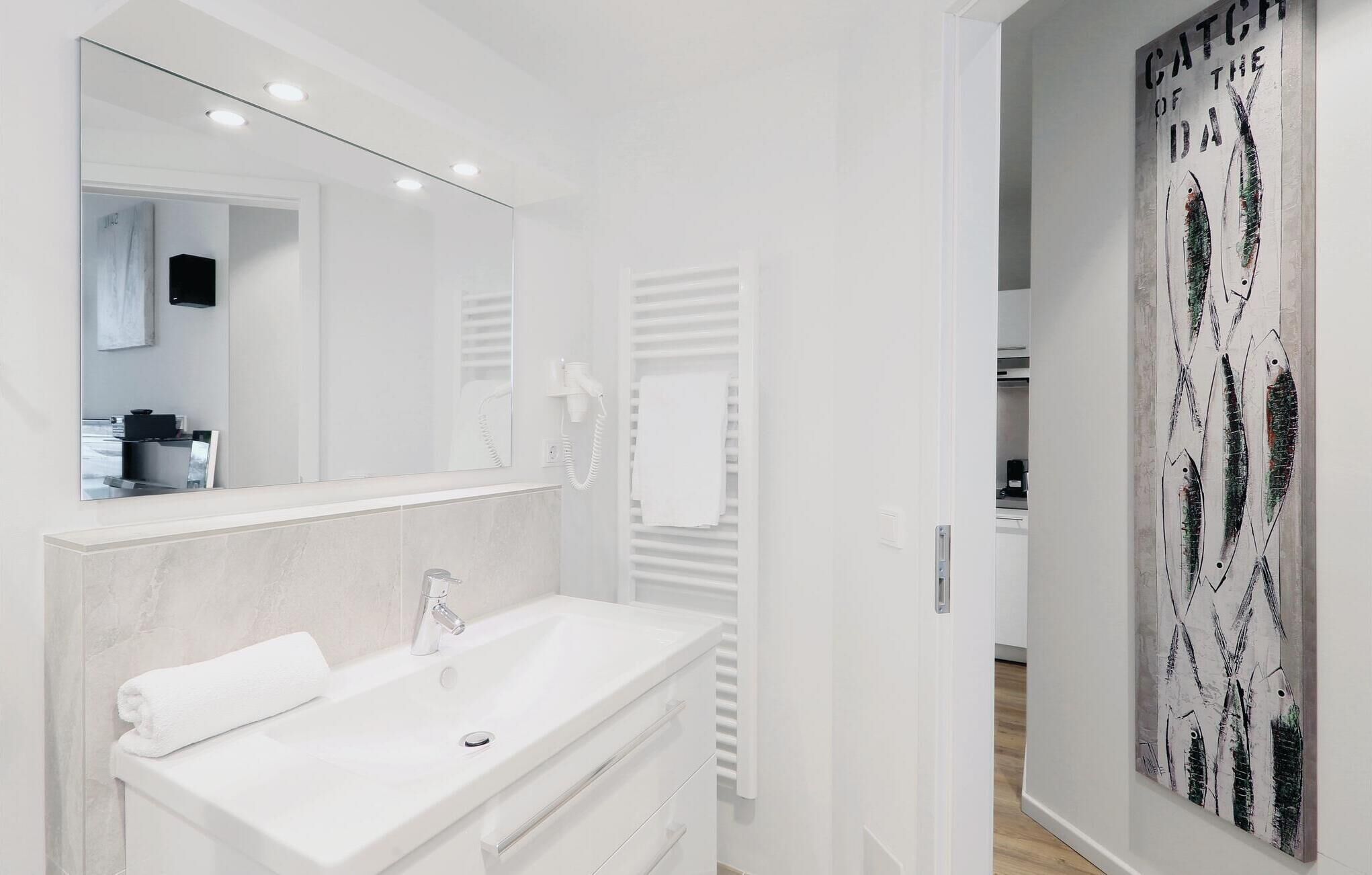 A modern bathroom with a white vanity, a large mirror, and a towel rack.