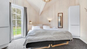 Een slaapkamer met een bed, een raam met gordijnen, een wandlamp, een spiegel en een witte kast.