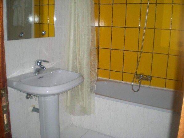 Un baño con lavamanos blanco, espejo, ducha con azulejos amarillos y bañera.