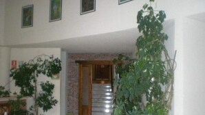 Un vaste espace de vie agrémenté d’un escalier menant à un deuxième étage, entouré de plantes en pot et de tableaux encadrés accrochés aux murs.