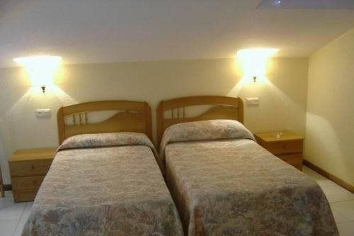Un dormitorio con dos camas individuales, cabeceros de madera, mesitas de noche y lámparas de pared.