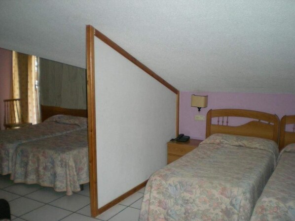 Habitación con dos camas individuales, un separador de madera, una mesita de noche con lámpara y un ventanal con cortinas.