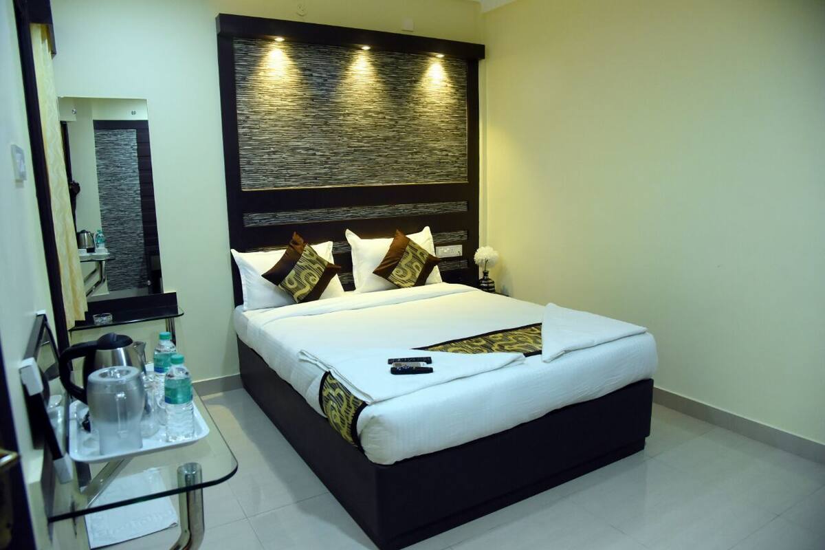 Una habitación de hotel con una cama grande, una mesita de noche con un neceser y una lámpara de pared sobre la cama.