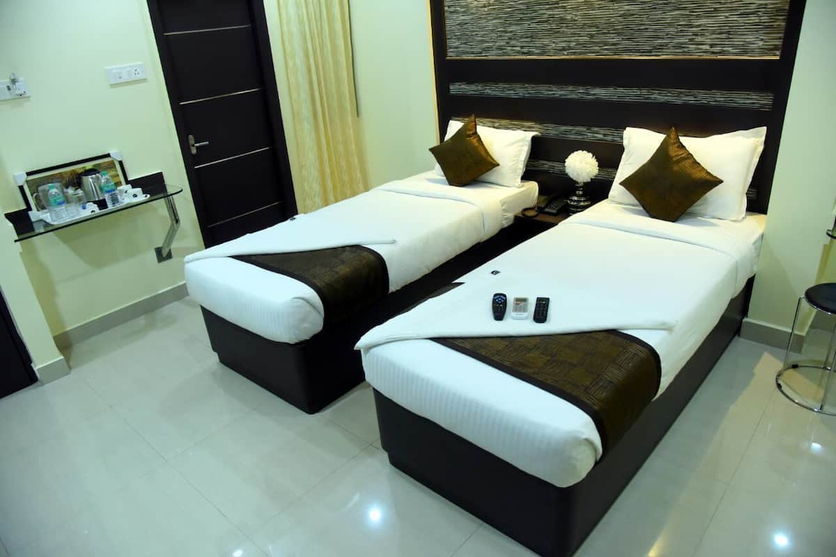 Una habitación de hotel con dos camas, una mesita de noche con lámpara y un estante con artículos de aseo.