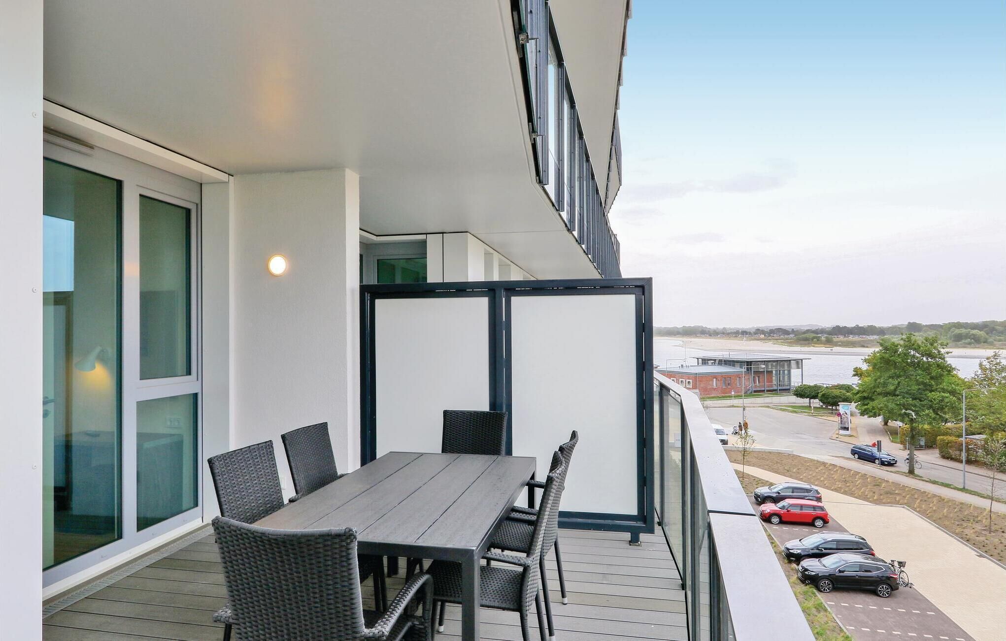 A balcony with a dining table and chairs, overlooking a parking area and a body of water.