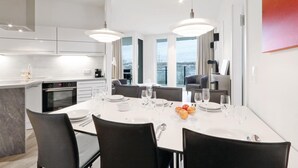 Et moderne spiseområde med et hvidt bord dækket til fire personer, sorte stole og udsigt over byen gennem store vinduer.