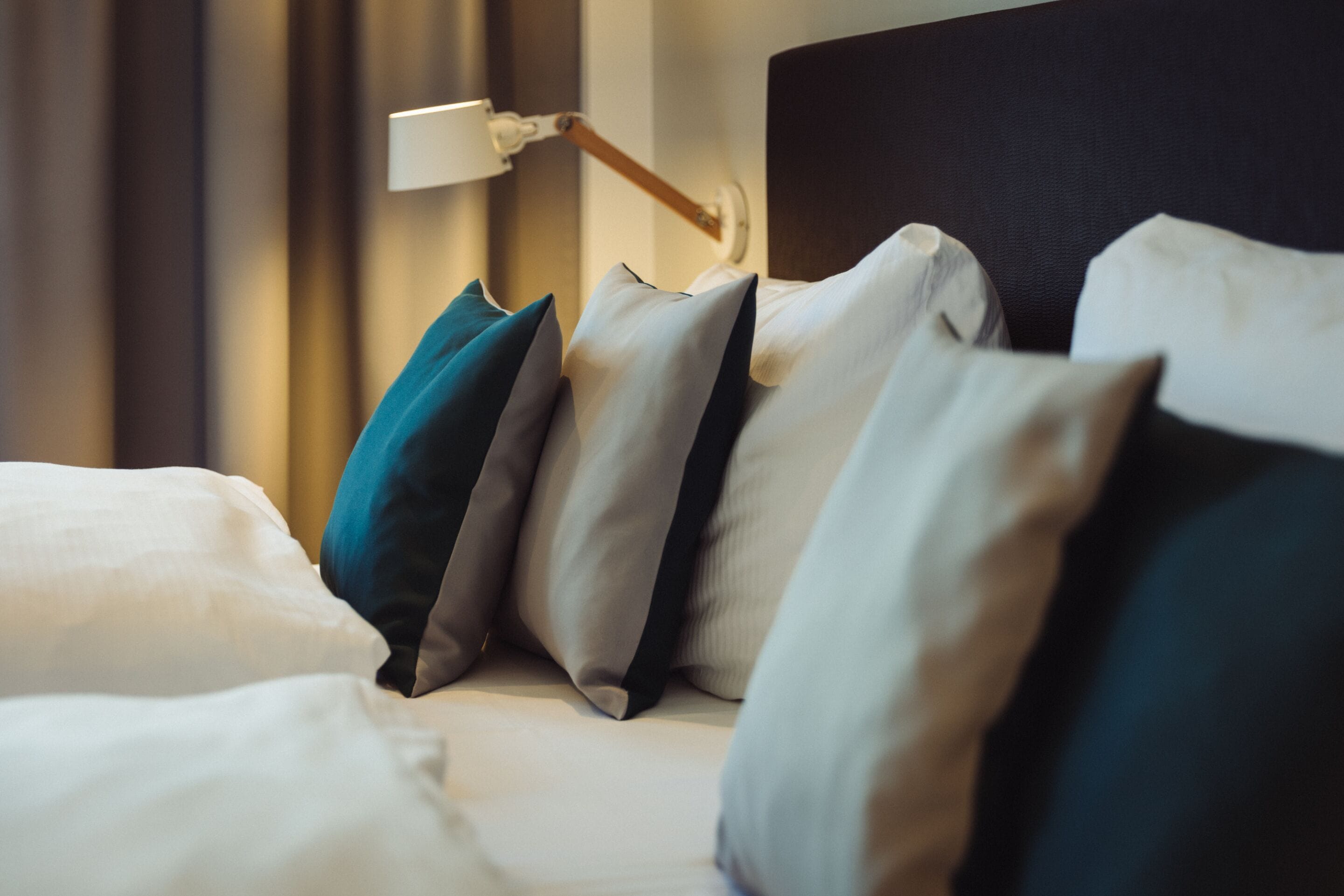 Una cama bien hecha con varios almohadones en tonos blanco, gris y aguamarina.