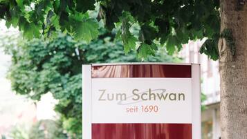 A sign with the text "Zum Schwan seit 1690" under a tree.