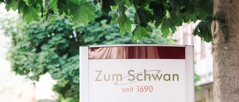 Un letrero con el texto "Zum Schwan seit 1690" bajo un árbol.