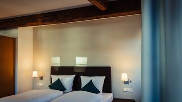 Ein Hotelzimmer mit zwei Betten, dunklen Kopfteilen, Nachttischlampen und einem Holzbalken an der Decke.
