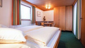 Une chambre d’hôtel avec deux lits, une petite table avec une chaise, une fenêtre avec des rideaux et une armoire en bois.