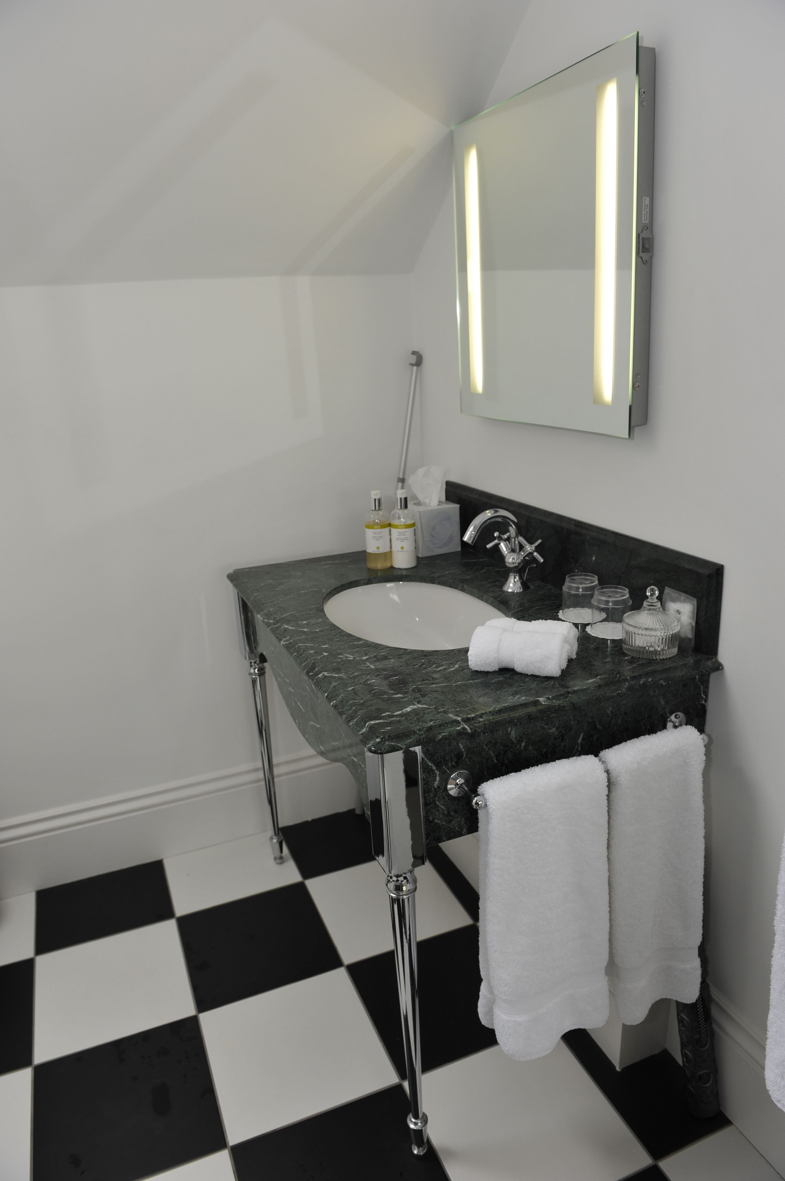 A bathroom with a black and white checkered floor, a white sink with a marble countertop, chrome fixtures, and two towels hanging on the wall.