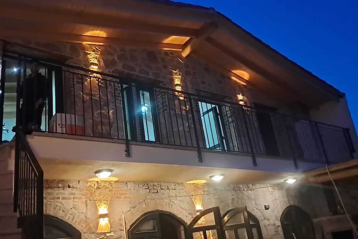 A two-story building with stone walls, a balcony with metal railings, and multiple windows.