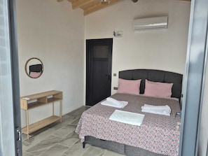 A bedroom with a bed, a bedside table, a mirror, a door, and an air conditioning unit.