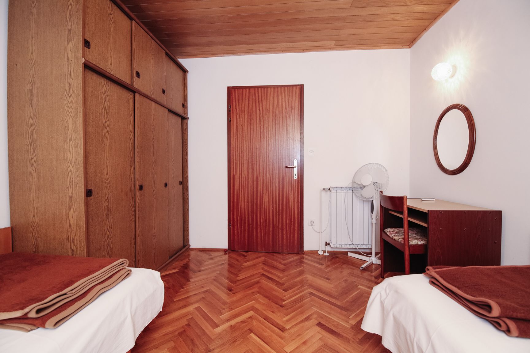 A bedroom with two beds, wooden wardrobe, radiator, and a mirror on the wall.