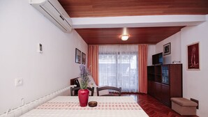 A room with a dining table, chairs, a red vase with flowers, a television, and a cabinet.