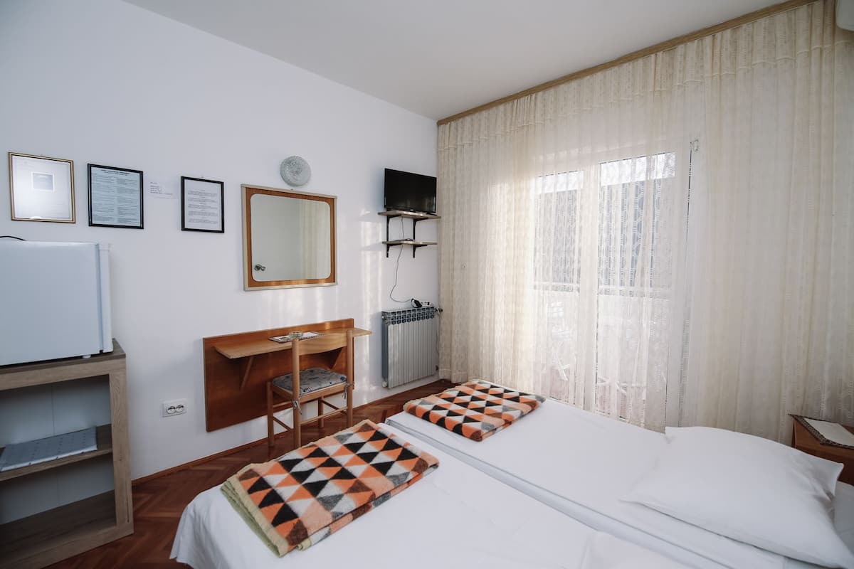 Habitación de hotel con cama, escritorio, silla, televisión y ventana con cortinas.