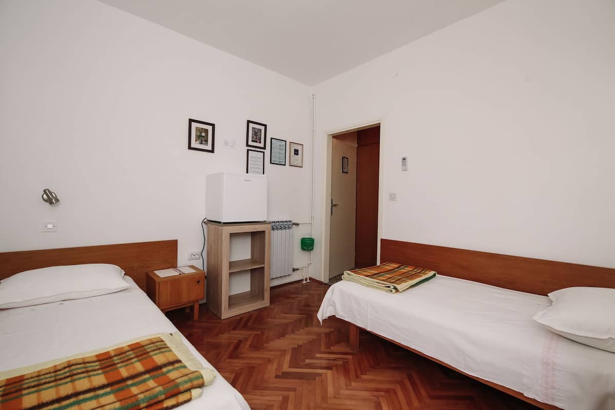 Habitación de hotel con dos camas, un armario de madera, un radiador y cuadros enmarcados en la pared.