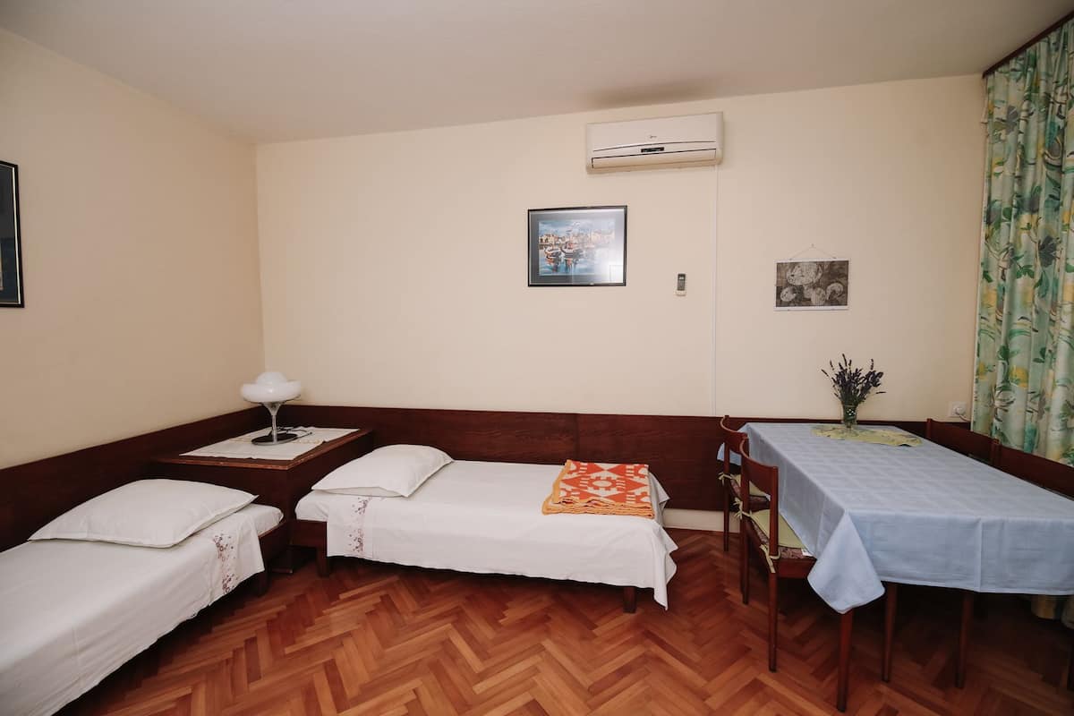 Una habitación con tres camas individuales, una mesa de comedor y una mesita de noche con una lámpara.