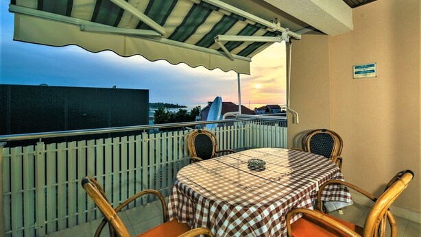 A balcony with a table and chairs, a view of the sunset, and a white fence.