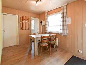 A room with a wooden dining table, four chairs, a whiteboard, and a window with curtains.
