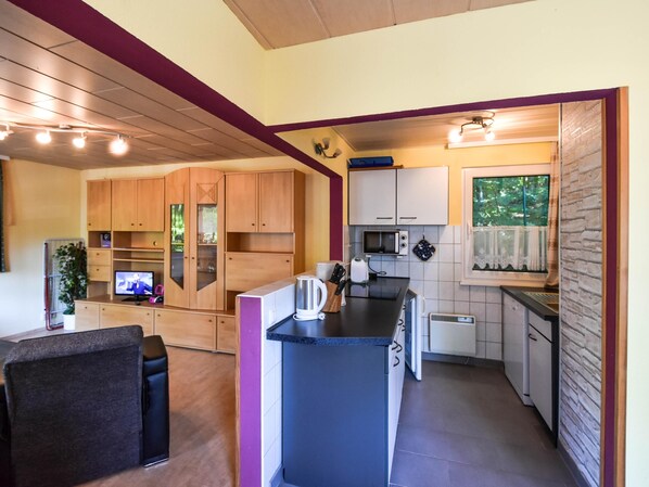 A compact kitchen with wooden cabinets, a microwave, a toaster, and a small dining area with a chair.