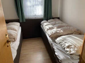 Ein Zimmer mit zwei Betten, Holzboden und einem Vorhangfenster.