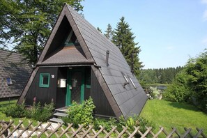 Ein dreieckiges Holzgebäude mit geneigtem Dach, einer grünen Tür und einer kleinen Veranda.