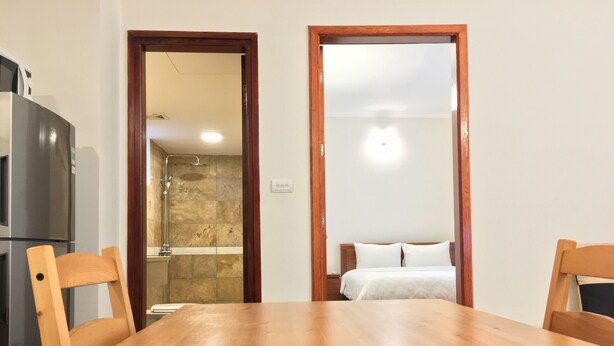 Ein Holztisch mit Stühlen, eine Küchenzeile mit Kühlschrank sowie ein Badezimmer mit Dusche und einem Bett.