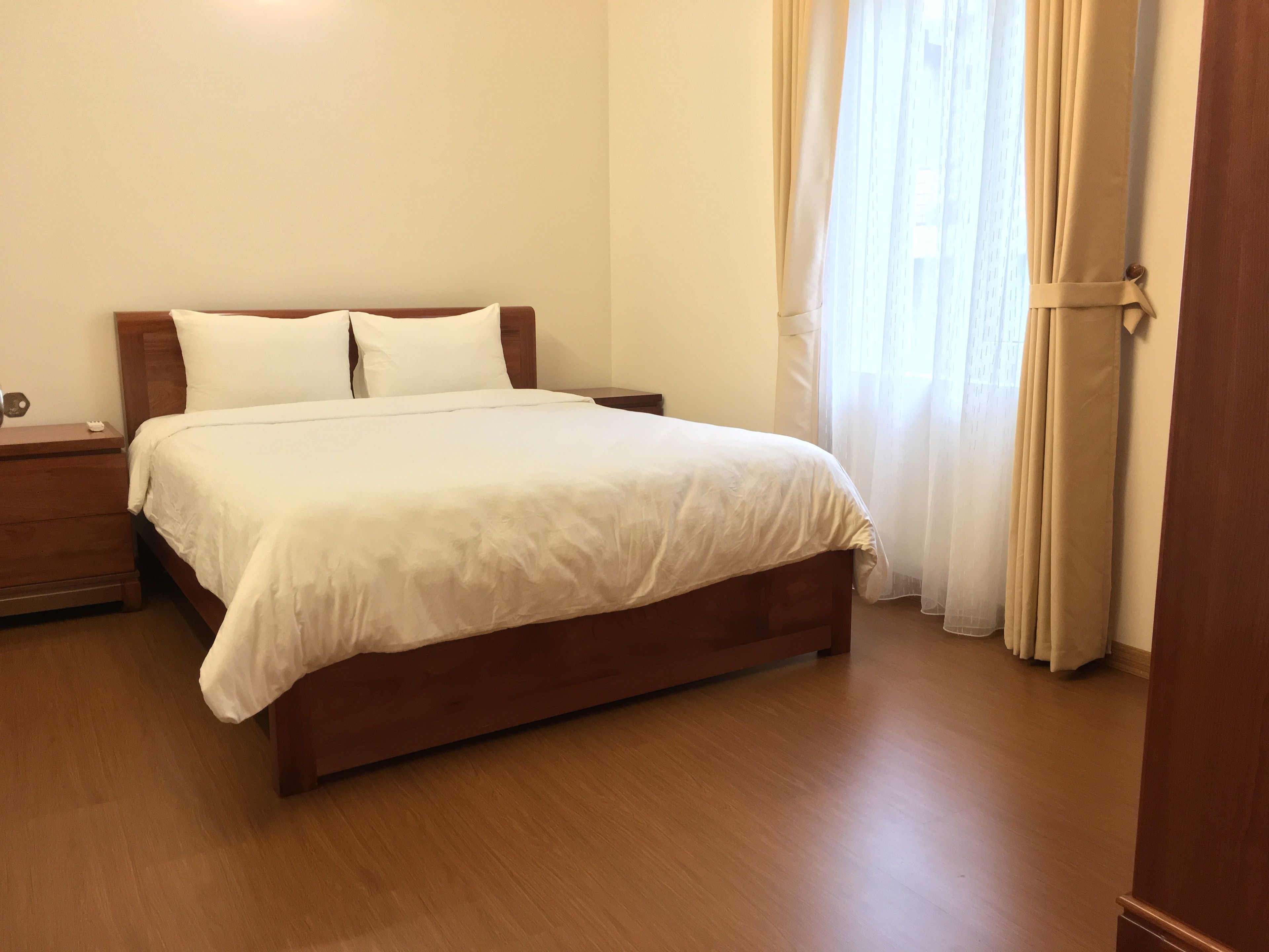 A neatly made bed with white linens in a room with wooden flooring and a nightstand.