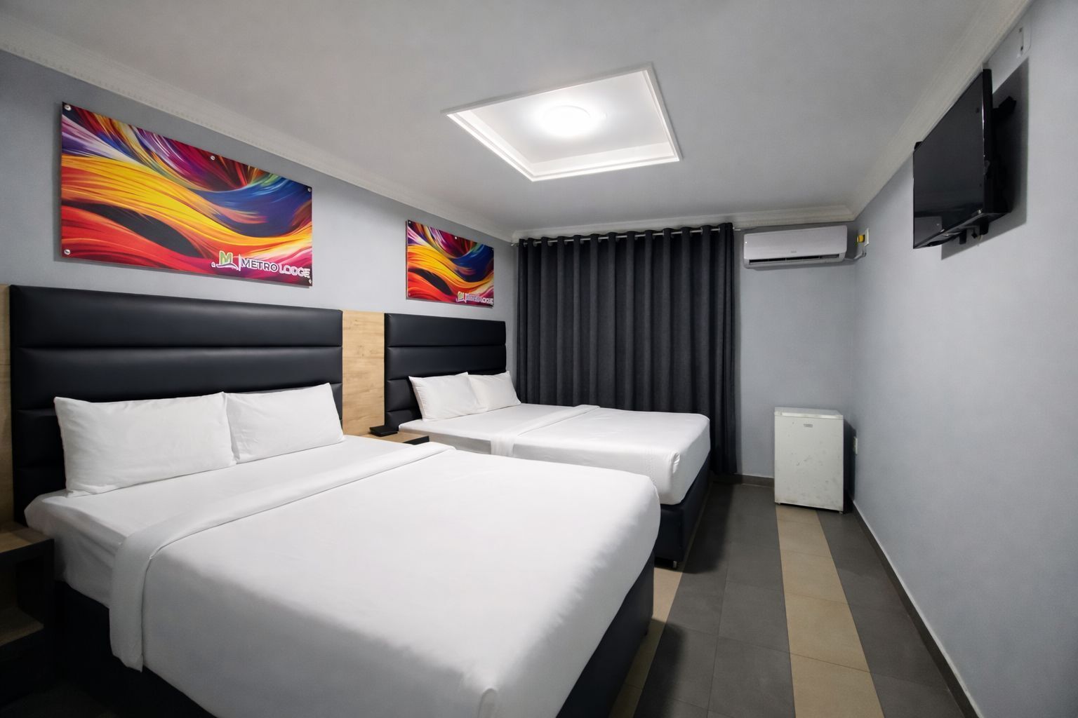 A hotel room with two beds, a flat-screen TV, an air conditioning unit, and two colorful abstract wall art pieces.