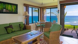 A room with a green sofa, wicker chairs, a wooden table, and a view of the ocean.
