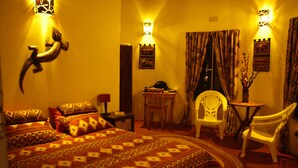 A room with a bed, two chairs, a small table, and a desk. There are wall-mounted lamps and curtains. - Sadadu (Nkomazi)