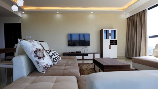 A modern living room with a sofa, a TV, a cabinet, and a large window with curtains. - Kileleshwa Lux Condo (Nairobi)
