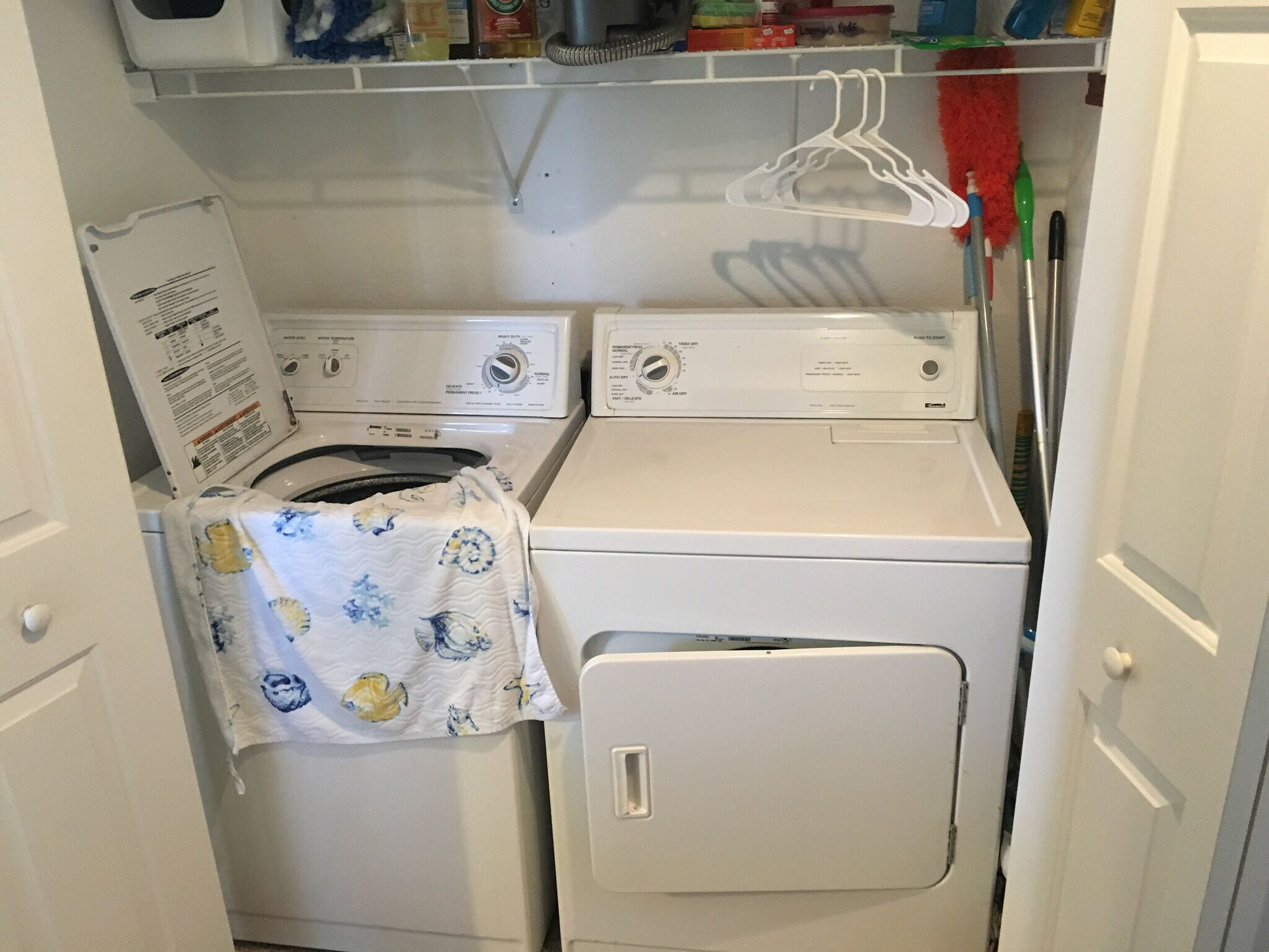 A laundry area with two washing machines and a dryer, a white door, and a shelf above the machines.