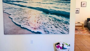 Ein großes Wandbild zeigt einen Strand bei Sonnenuntergang, einen gefliesten Boden und einen Wäschekorb mit Kleidung.