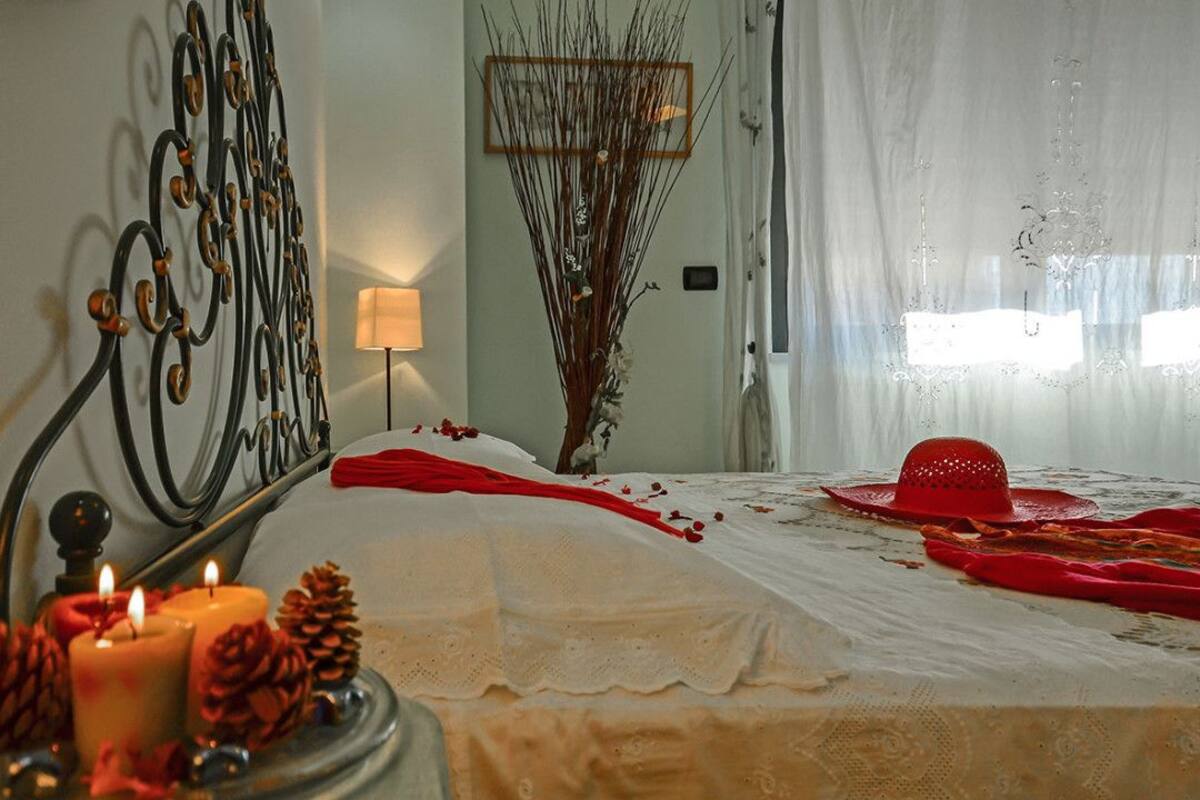 A bedroom with a bed, candles, pine cones, and a decorative hat on the bed.