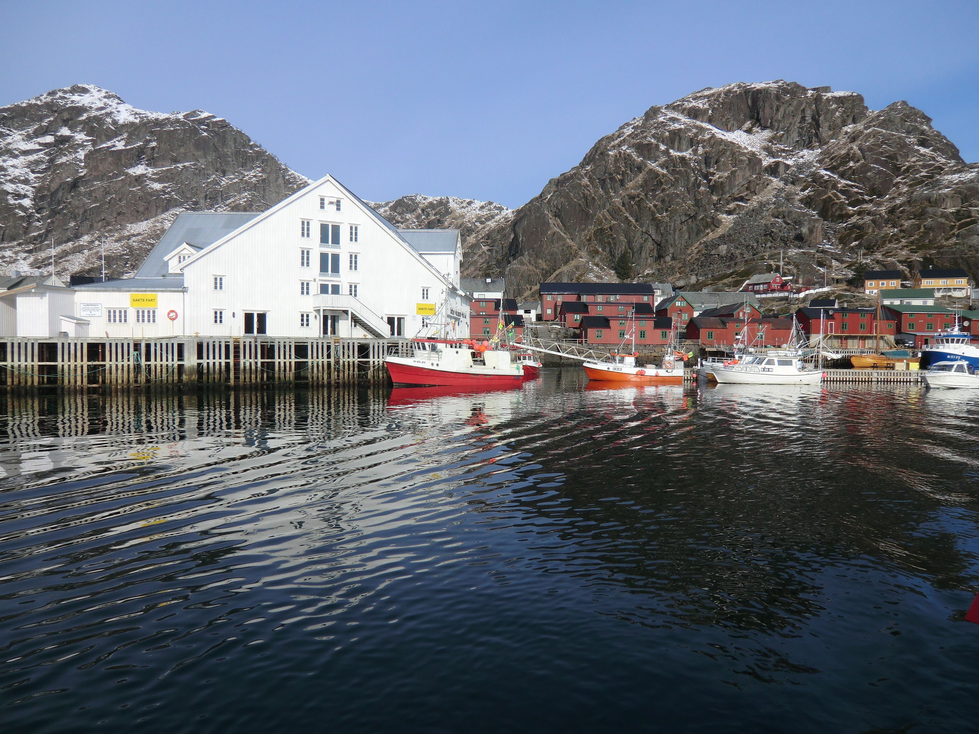 A harbor with boats, a white building with multiple windows, and a mountainous backdrop.