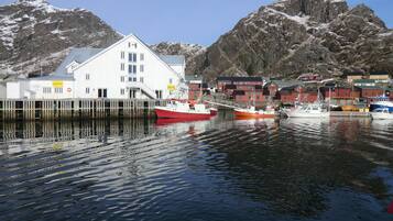 A harbor with boats, a white building with multiple windows, and a mountainous backdrop.