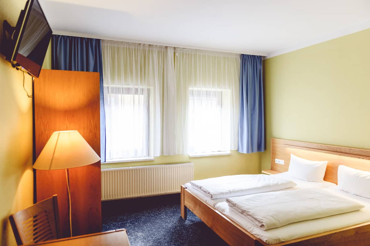 Une chambre d’hôtel avec deux lits, un bureau, une lampe et un téléviseur fixé au mur.