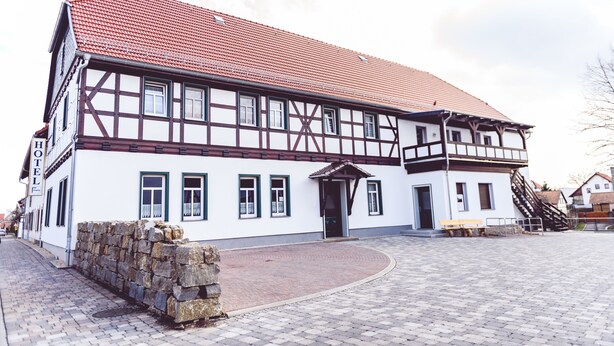 A traditional half-timbered building with a red-tiled roof, a stone wall, and a paved courtyard with benches. - Landgasthof Schwabhausen (Schwabhausen)