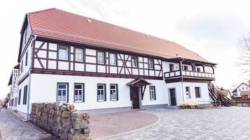 A traditional half-timbered building with a red-tiled roof, a stone wall, and a paved courtyard with benches.