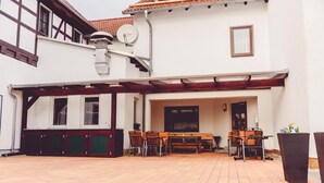 A building with a covered patio area featuring a wooden table and chairs, a satellite dish, and a door leading to an interior space. - Landgasthof Schwabhausen (Schwabhausen)