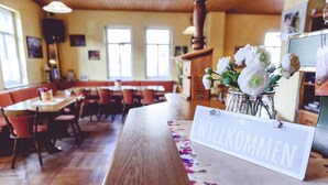 A restaurant interior with wooden tables and chairs, a 'Willkommen' sign, and a vase of white flowers. - Landgasthof Schwabhausen (Schwabhausen)