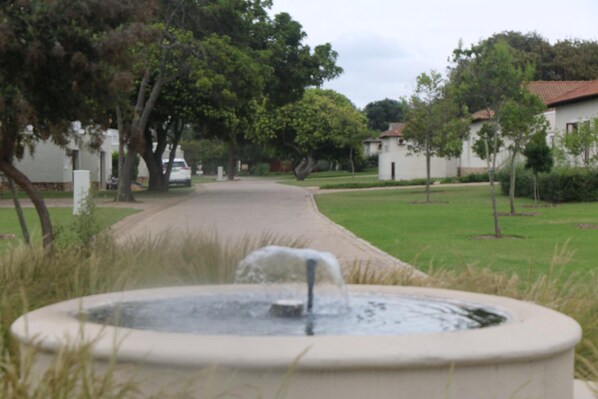 A fountain in a landscaped area with a pathway leading to a row of houses. - The Dunes Resort 80 (Keurboomstrand)