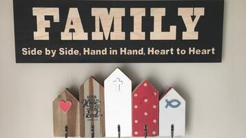 Et ophængt skilt med ordet 'FAMILY' og teksten 'Side om side, hånd i hånd, hjerte til hjerte' over en række træhuse-formede kroge med forskellige symboler og tekst.